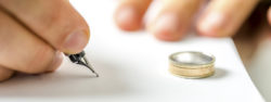 Closeup of male hand signing divorce papers.